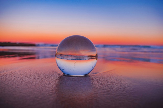 A glass orb resting on the sand reflecting an inverted sunset over the ocean — a metaphor for seeing your future self differently